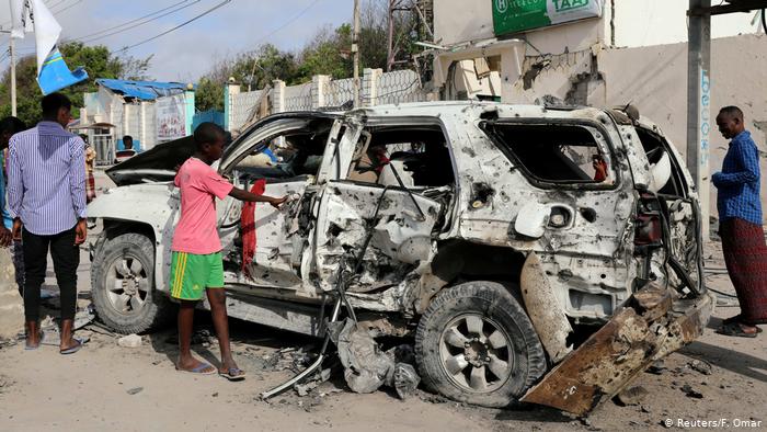 Civilians are seen near the wreckage of a car destroyed at the scene of a militant attack at the Elite Hotel in Lido beach, Mogadishu